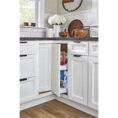 an open cabinet in a kitchen with white cabinets and wood flooring on the walls