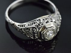 This Art Deco engagement ring has no shortage of charming details. Lacey, beaded scrolls and criss-cross patterns cover the whole top of the ring making it light and airy. It is crowned with a glittering diamond held in place by 8 tiny prongs. It would make an excellent engagement or vintage statement piece! * Art Deco 1930's approximately * 18K White gold * .07ct (approximate) Transitional cut diamond * Size 6.5 - Can be resized within a couple sizes * Very good/excellent condition - Some wear Vintage White Gold Promise Ring Jewelry, Victorian Platinum Rings As Gifts, Oval Platinum Jewelry With Intricate Design, Victorian 14k White Gold Formal Jewelry, Antique Filigree Engraved Ring For Anniversary, Victorian 14k White Gold Jewelry For Formal Occasions, Classic Engraved Filigree Ring For Formal Occasions, Elegant Filigree Ring With Intricate Design For Marriage, Antique Jewelry With Intricate Round Cut Design