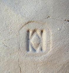 the letter m is inscribed in sand with a diamond on it's left side