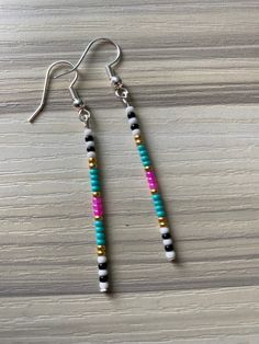 two long beaded earrings sitting on top of a wooden table