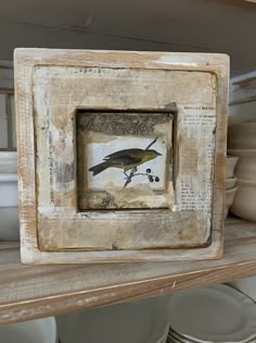 an old wooden frame with a bird painted on the inside is sitting on a shelf