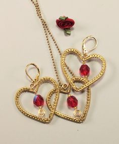 "This set of gold-toned heart earrings and necklace is embellished with sparkly red fire-polished crystal beads that flash blue and red when the light hits them. After shaping. they were woven with a fine non-tarnish gold-tone wire, and the bead dangles were added as a finishing touch.  The earrings have latch-back ear wires, and the ball necklace chain is 18\" long. Each piece is 1.25\" wide by 1 1.8\" tall. Will make a great Valentine's day gift for someone special, or just to show your love anytime of the year." Nickel Free Gold Heart Shaped Jewelry, Metal Jewelry For Valentine's Day Party, Mother's Day Party Jewelry With Open Heart Shape, Valentine's Day Open Heart Jewelry For Party, Valentine's Day Open Heart Party Jewelry, Open Heart Jewelry For Valentine's Day Jewelry Making, Handmade Open Heart Jewelry For Valentine's Day, Heart Beads Metal Earrings For Gift, Gold Dangle Jewelry With Heart Beads