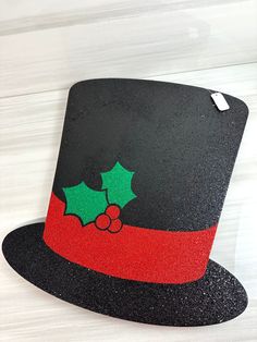 a black and red hat with holly berry on the top, sitting on a white table