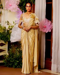 The flower patch on the shoulder seems like it is blooming from the joy of the season. The draped saree made with lightweight fabric materializes the concept of a fairy. The gold saree is embellished with beadwork and applique flowers all around to appear as if standing amongst flowers. Cold shoulder style blouse with back hook Pre-draped saree with a flower patch on the shoulder accentuated with beads and sequins embroidery. Metal zip on the saree. From Moledro’s Taabir collection. DELIVERY TIM Beads And Sequins Embroidery, Gold Saree, Applique Flowers, Draped Saree, Cold Shoulder Styles, Drape Saree, Flower Patch, Style Blouse, Sequins Embroidery