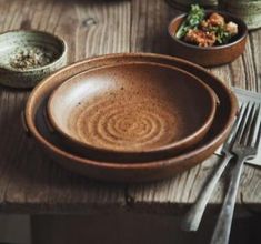 a wooden table topped with plates and bowls filled with food next to utensils