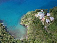 an aerial view of a house on the edge of a cliff with blue water and trees surrounding it