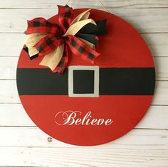 a red and black santa clause sign hanging on a white wooden wall with a bow