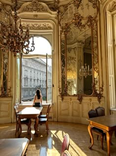 a woman is sitting at a table in an ornate room with mirrors and chandeliers