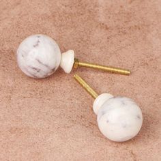 two white marble ball and gold plated screws on carpeted area with beige background