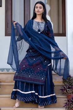 This is 3 piece set.It comes with bandhani print kurta teamed with flared sharara and a dupatta to match. 3 Piece Set Fabric-Cotton Color-Navy Blue Work-Bandhani print, embroidered, sequins work with front & side tassels Kurta Detailing-Calf length kurta with side slits Bottom-Flared Sharara Sleeves-3/4th Sleeves Neck-Round Neck Occasion-Festive wear Washing care-Hand wash Blue Sharara With Straight Kurta For Festive Occasions, Festive Blue Sharara With Straight Kurta, Traditional Blue Palazzo Set With Mirror Work, Designer Georgette Palazzo Set With Bandhani Print, Blue Bollywood Sharara For Transitional Season, Traditional Blue Palazzo Set, Blue Straight Kurta Palazzo Set For Festivals, Blue Palazzo Set For Festivals, Blue Sharara With Chikankari Embroidery For Transitional Season