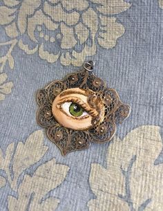 "Hand-painted Lover's Eye vintage silver filigree pendant. This piece of jewelry is a one of a kind, hand-painted by me on a vintage piece of jewelry selected also by me. It's painted with acrylic paint and varnished for protection and signed on the inside of the pin. The pendant is 1 3/4 wide x 1 1/2 inch wide. It comes with a silver plated chain - 18 inches long. \"The lover's eye is an 18th century variation on a portrait miniature of a secret love which typically displayed only the eye and e Vintage Pendant Necklace With Artistic Design, Vintage Pendant Necklaces With Artistic Design, Handmade Antique Enamel Necklaces, Collectible Bohemian Jewelry With Artistic Design, Vintage Hand Painted Round Pendant Necklace, Bohemian Hand Painted Jewelry For Art Collection, Vintage Enamel Jewelry With Filigree Details, Vintage Enamel Jewelry With Filigree, Vintage Hand-painted Pendant Necklace