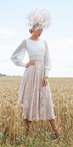 a woman standing in a wheat field wearing a dress and hat with feathers on it