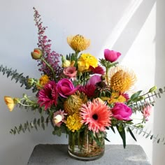 a vase filled with lots of different colored flowers on top of a table next to a white wall