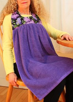 a woman sitting in a chair with a purple blanket on her lap and she is looking at the camera