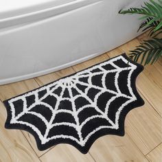 a black and white spider web rug in front of a bathtub with a potted plant