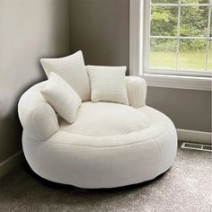 a white chair sitting in front of a window with pillows on top of the seat