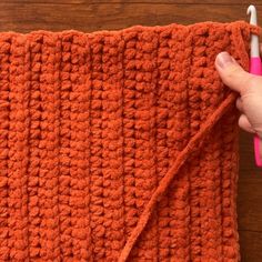 someone is crocheting the edges of an orange blanket with a pink toothbrush