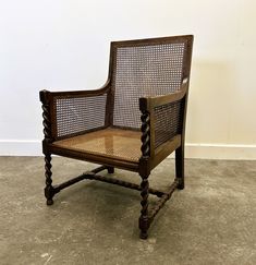 an old wooden chair with wicker back and arms on concrete floored area next to white wall