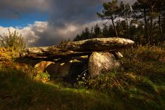 a large rock sitting on top of a lush green hillside under a cloudy blue sky