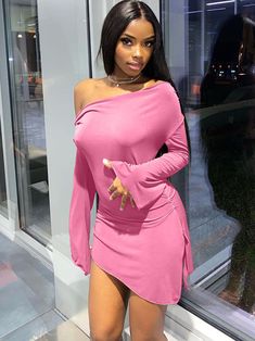 a woman in a pink dress posing by a window with her hands on her hips