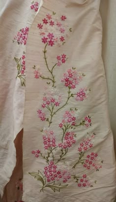 a white sheet with pink flowers and green leaves on it, sitting next to a wall