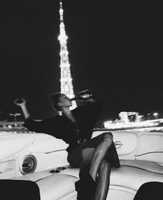 a woman sitting on top of a car in front of the eiffel tower