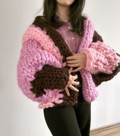 a woman wearing a pink and brown knitted jacket with her hands on her hips