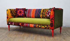 a green couch with colorful pillows on it's back and legs, sitting in front of a white wall