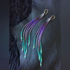 purple and green beaded earrings on a black leather surface with dark furnishing