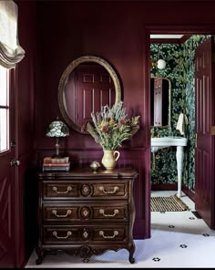 a room with red walls and a dresser in the corner, along with a mirror