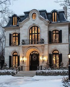 a large white brick house with black shutters and lights on the front door is covered in snow