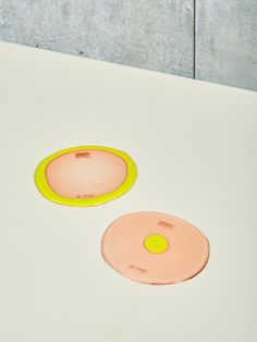 two yellow and pink plates sitting on top of a white table next to each other