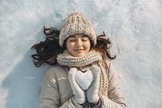 a woman wearing a hat and scarf with her eyes closed while laying in the snow