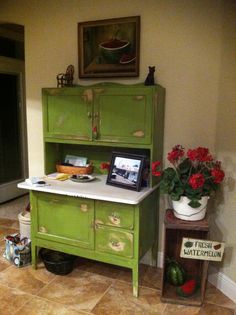 a green cabinet sitting in the corner of a room next to a potted plant