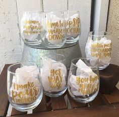 wine glasses with gold foil lettering on them sitting on a wooden table next to a barrel