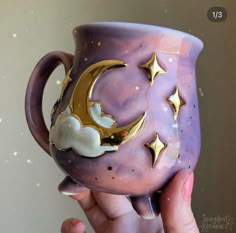 a hand holding a purple coffee cup with gold stars and moon decorations on it's side