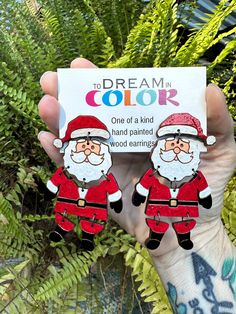 someone holding up two santa claus earrings in their hand with the caption to dream in color