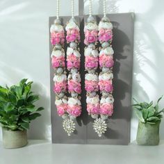 pink and white flowers hanging from hooks on a gray wall next to potted plants