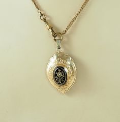 A charming antique Victorian locket back shield shaped pendant with a 14K gold front with black enamel and seed pearl. The center with an oval black enamel panel with a very lovely gold rose of Sharon or possibly a pansy flower and foliage set with a seed pearl, 1mm in diameter, with a gold band and black enamel outer border. With embossed trailing husks and forget-me-not. With a finely beaded outer border. The reverse in acid tested silver with a glazed opening panel and the remains of the orig Victorian Black Enamel Pendant Jewelry, Black Engraved Necklace For Wedding, Victorian Engraved Rose Gold Locket Necklace, Ornate Engraved Locket Necklace For Formal Occasions, Ornate Engraved Locket Necklace For Formal Events, Ornate Locket Necklace For Formal Occasions, Antique Gold Necklaces With Black Enamel, Victorian Rose Gold Locket Necklace, Antique Black Locket Jewelry