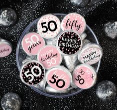 a glass bowl filled with pink and black 50th birthday buttons on top of silver foil