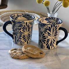 two blue and white mugs sitting on top of a table next to a cookie