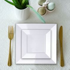 an empty white plate on a table with gold utensils