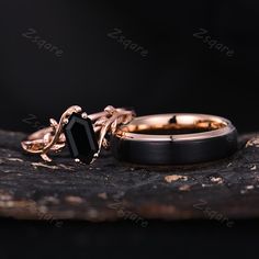 two gold rings with black onyxite stones sitting on a piece of wood next to each other