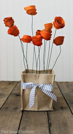 some orange flowers are in a burlock vase on a wooden table with a bow