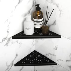 two black shelves with bottles and soap on them in a bathroom area that has white marble walls