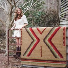 a woman standing next to a quilt on a metal rack in front of a house