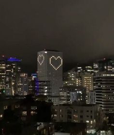 the city skyline is lit up at night with hearts drawn on it's windows