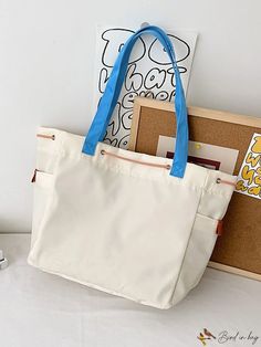 a white bag with blue handles sitting on top of a table next to a book