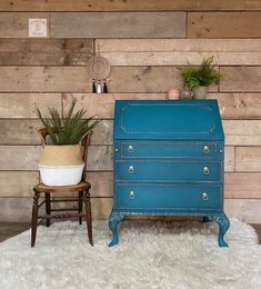 a blue chest of drawers next to a chair and potted plant on a white rug