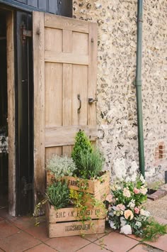 two wooden boxes filled with flowers next to an old door and brick walkway in front of a stone building